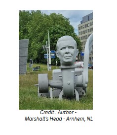 George Marshall's Head is shown in a kind of grey contraption - displayed in a green field, with trees beyond, in Arnhem, NL